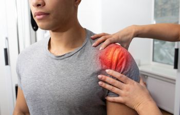 A doctor examining man's painful shoulder.