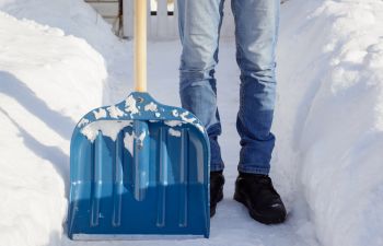 Young man after shoveling snow in front of the house standing in a narrow path with big snowbanks at both sides.
