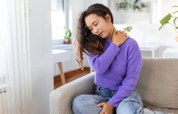 Asian woman suffering from backache and shoulder pain at home. Lower Back Pain . Woman feels back pain massaging aching muscles, sad woman suffers from low-back