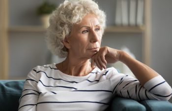 Pensive middle-aged old lady sit on couch at home look in distance thinking pondering, thoughtful unhappy elderly woman lost in thoughts missing remembering past, feeling lonely, solitude concept